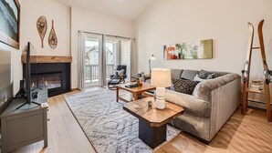 A living room with a fireplace, a sofa, a coffee table, and a TV. - 2 Bedroom Townhome with Private Garage!! (Frisco)