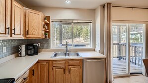 A kitchen with wooden cabinets, a coffee maker, and a window with a view of trees and a deck. - 2 Bedroom Townhome with Private Garage!! (Frisco)