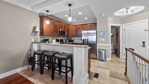 A modern kitchen with wooden cabinets, stainless steel appliances, and a bar area with stools. - Coast Time 2 Bedroom Condo at Croatan Surf Club (Kill Devil Hills)