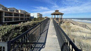 A wooden boardwalk leading to a beach with a gazebo, overlooking a row of multi-story buildings with balconies. - Coast Time 2 Bedroom Condo at Croatan Surf Club (Kill Devil Hills)