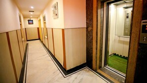Un pasillo con suelo de mármol, un ascensor y una televisión montada en la pared.