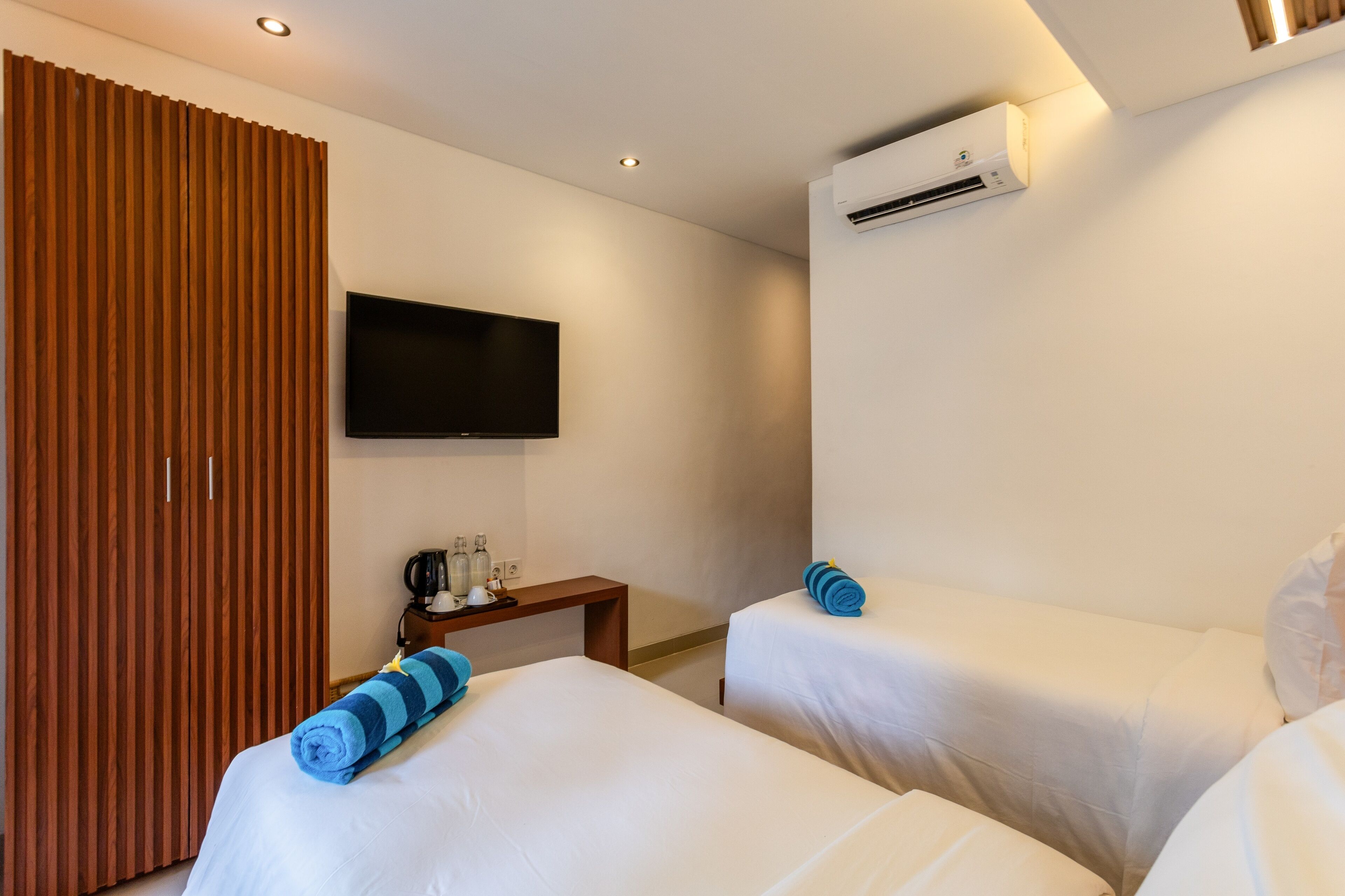 A hotel room with two beds, a TV, an air conditioner, and a wooden panel wall.
