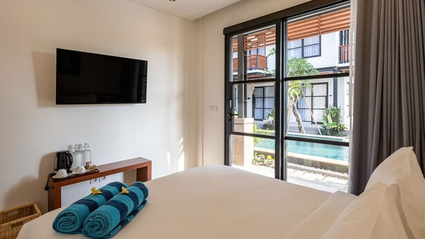 A hotel room with a large bed, a flat-screen TV mounted on the wall, a small table with toiletries, and a view of an outdoor swimming pool. - Paripadi Studio Canggu (Canggu)