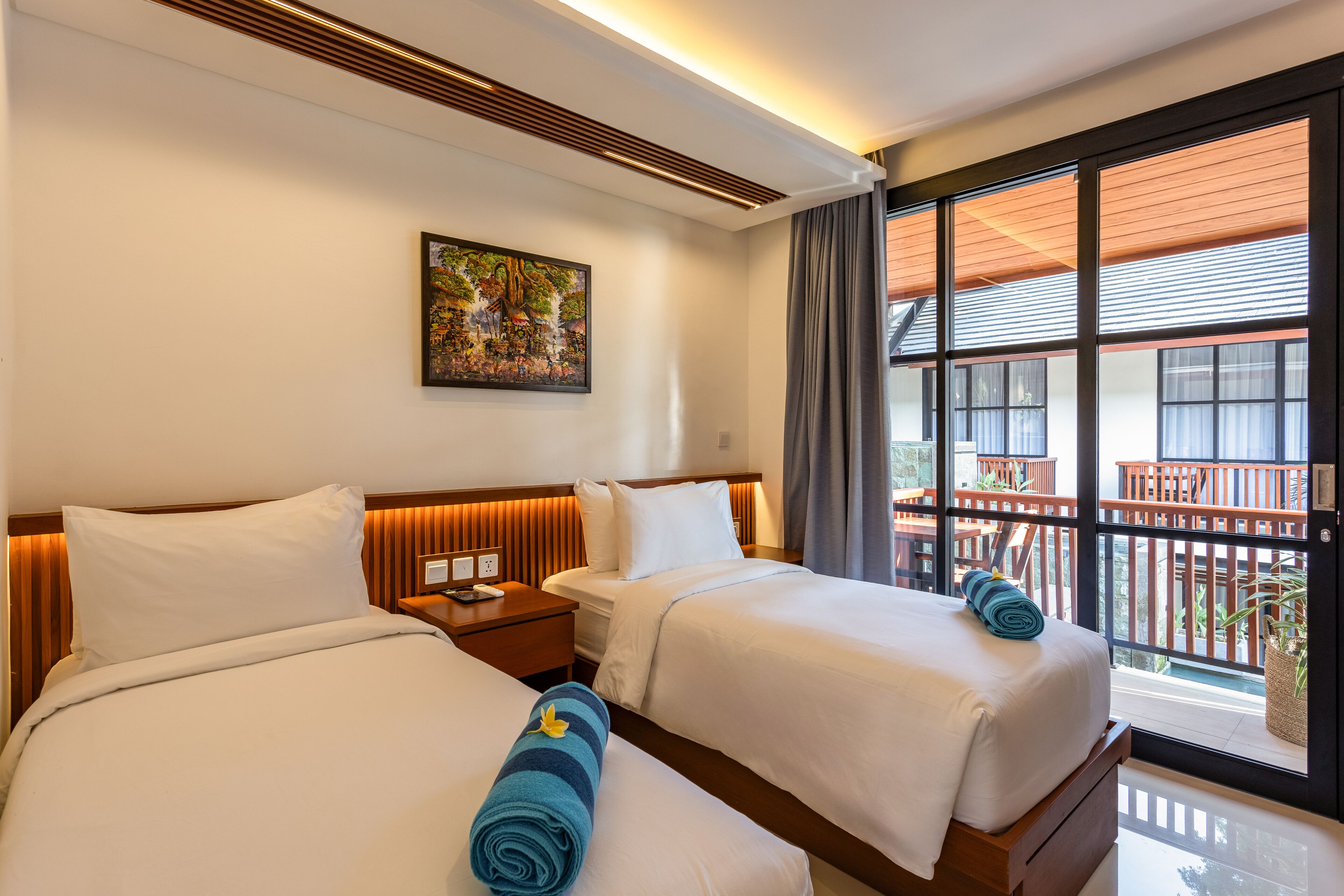 A hotel room with two beds, a painting on the wall, and a balcony with a view.