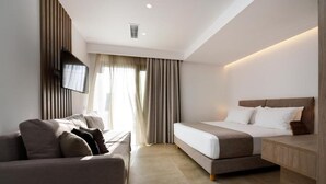 Une chambre d’hôtel moderne, équipée d’un lit, d’un canapé, d’un téléviseur fixé au mur et d’une fenêtre avec des rideaux.
