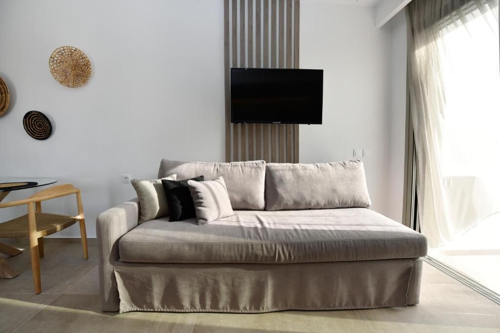 A modern living room with a sofa, a flat-screen TV mounted on the wall, and a dining table with chairs.