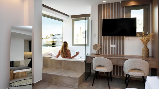 Une salle de bain moderne dotée d’une baignoire, d’un meuble-lavabo avec un téléviseur à écran plat et offrant une vue sur la ville.