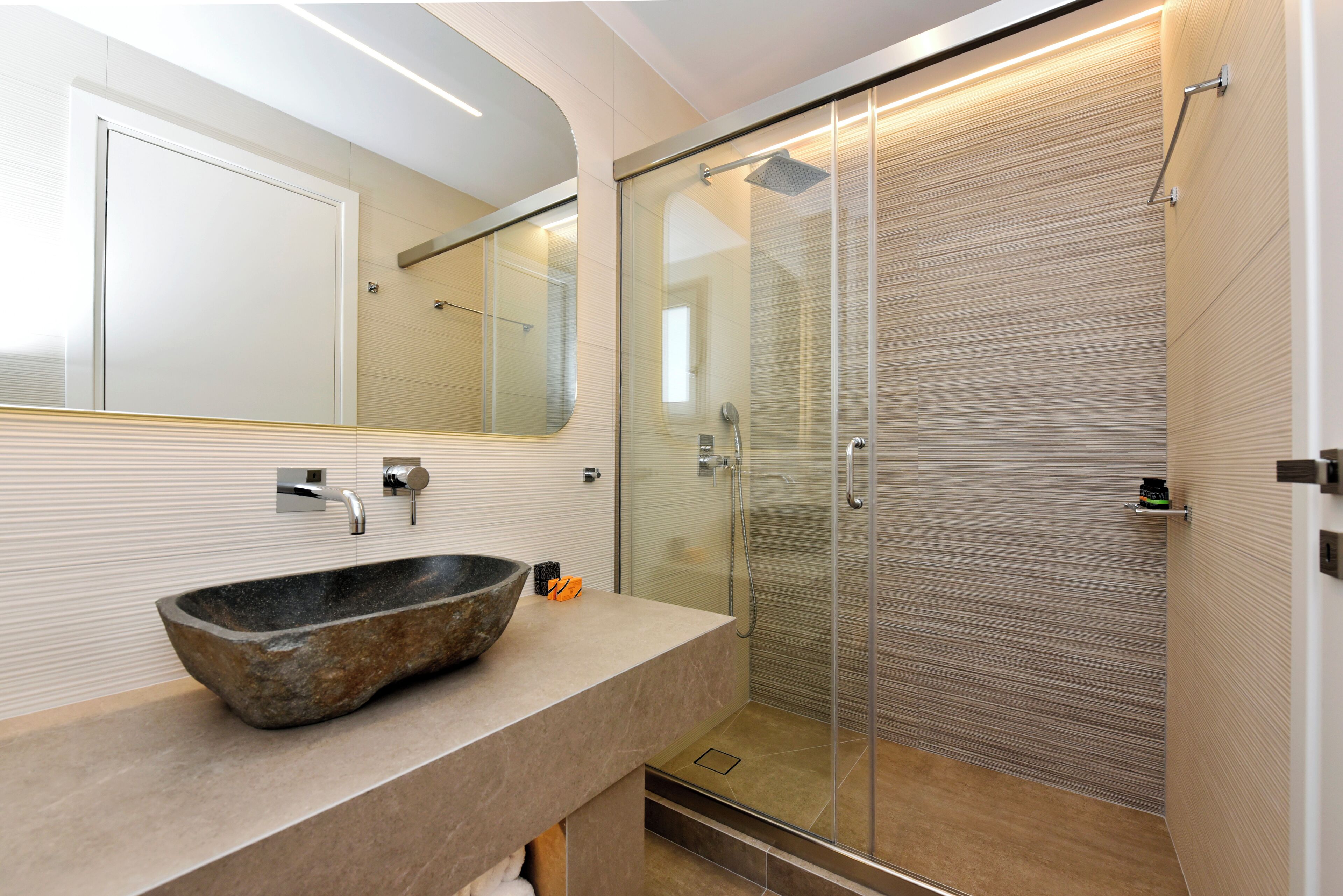 Une salle de bain moderne avec un lavabo en pierre, une douche en verre et un grand miroir.