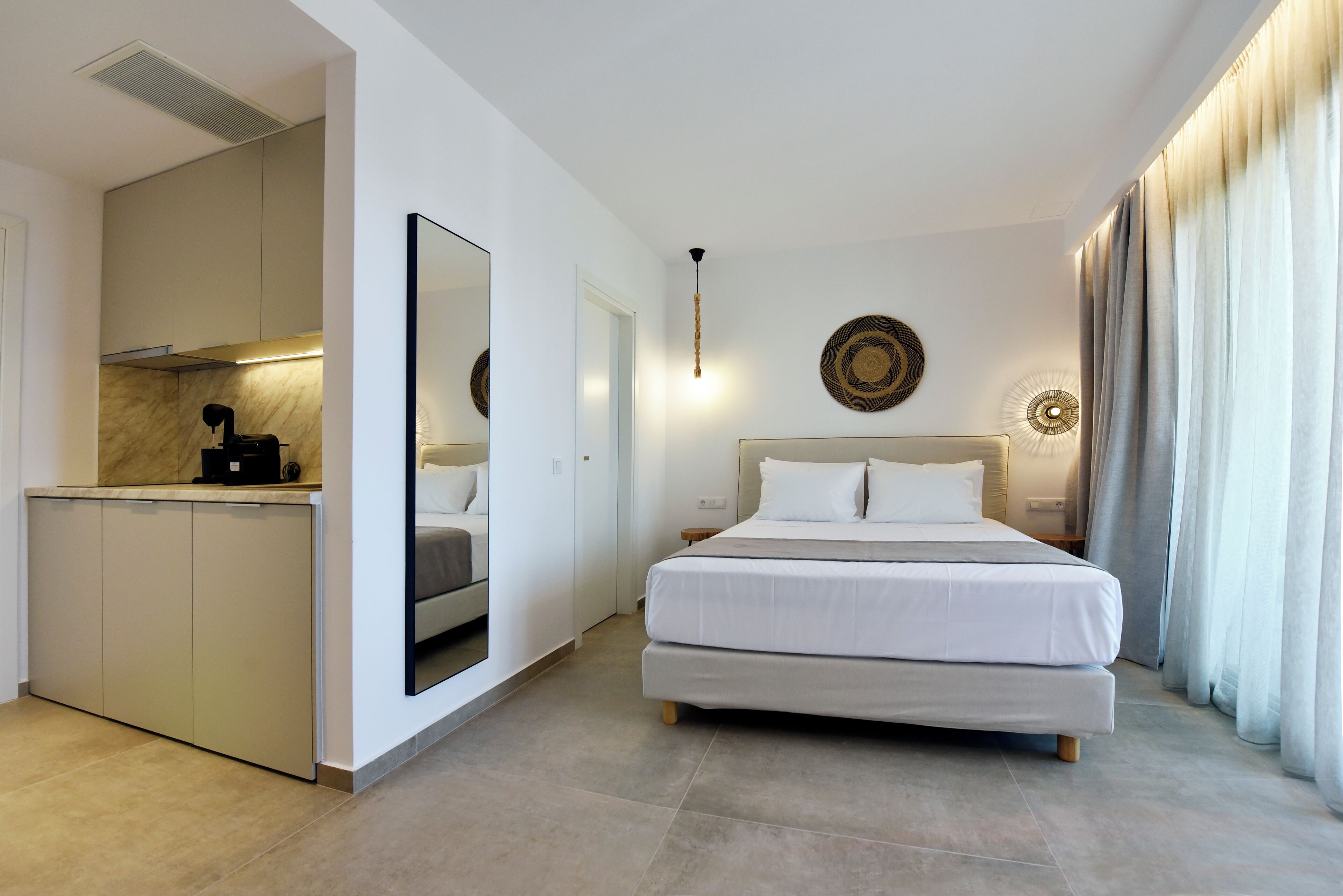 A modern hotel room with a large bed, a small kitchenette, and a bathroom visible through an open door.