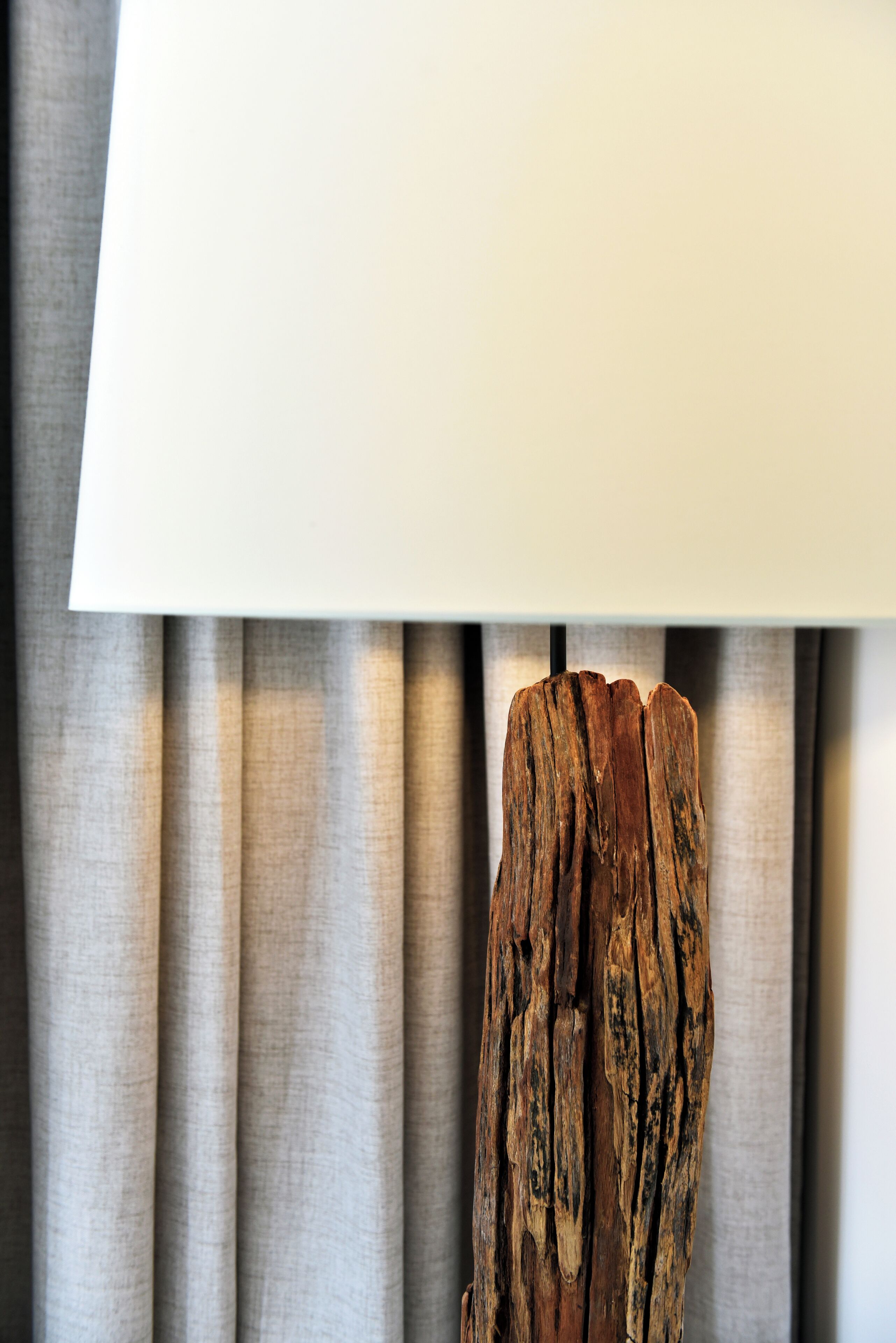 En lampa med en träbas och en vit lampskärm, placerad framför en draperad bakgrund.