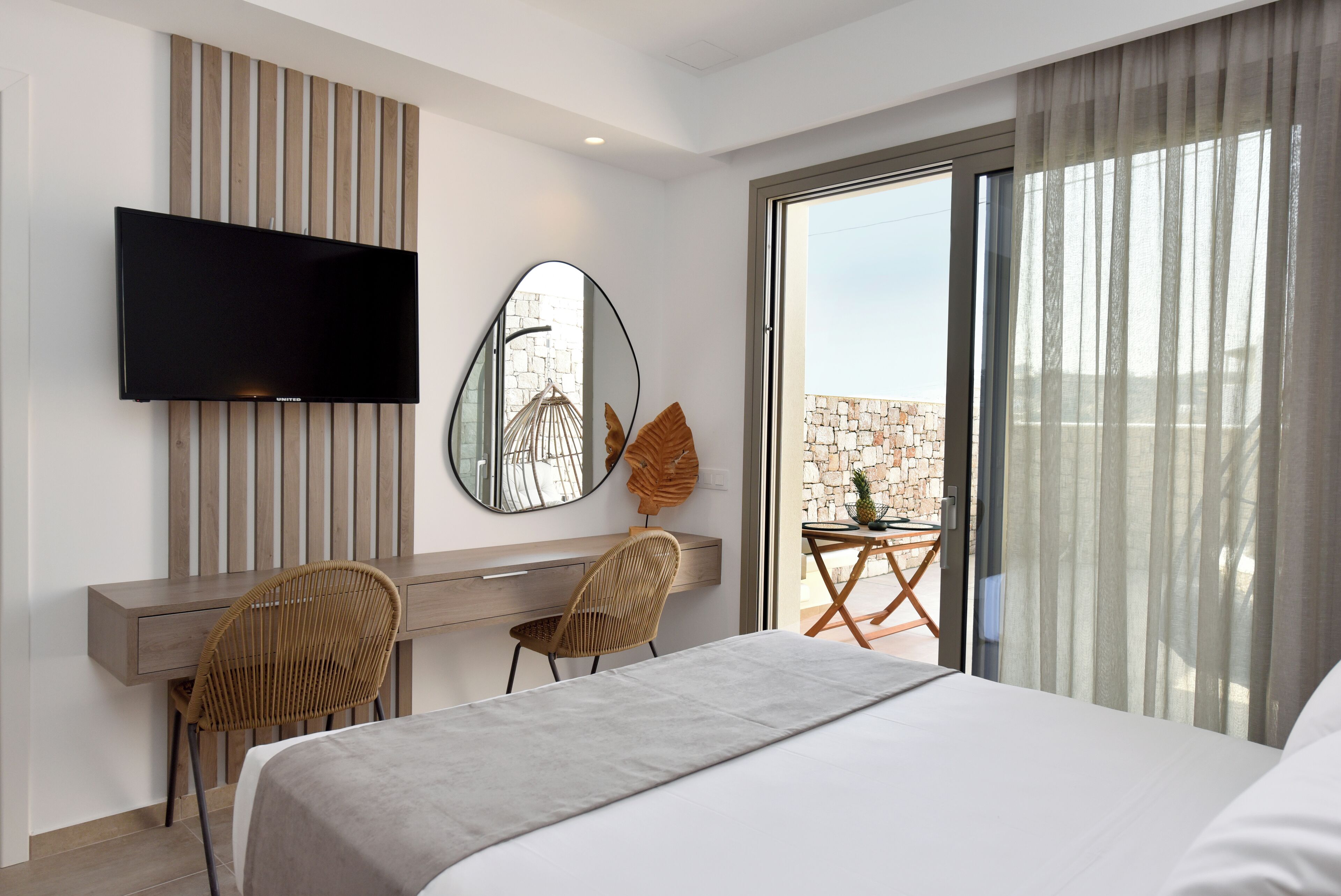 Une chambre d’hôtel moderne dotée d’un grand lit, d’un bureau avec deux chaises, d’une télévision à écran plat et d’un balcon offrant une vue sur la ville.