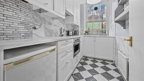 Une cuisine moderne avec des armoires blanches, un dosseret en marbre et un carrelage à motifs carrés.