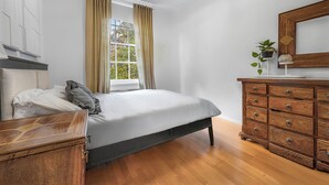 Une chambre à coucher avec un lit, une commode, une fenêtre avec des rideaux et une plante posée sur la commode.