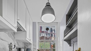Une cuisine avec des meubles blancs, un sol à carreaux noirs et blancs, une fenêtre donnant sur la ville et un luminaire suspendu.