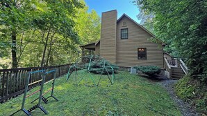 A wooden cabin with a sloped roof, surrounded by dense trees and a grassy yard. - Colston Creek- Nestled in the Trees with a beautiful creekside space (Bryson City)