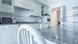A modern kitchen with white cabinetry, a granite countertop, a microwave, an oven, and a dining area with white chairs. - Italianway - Bodio 6 (Milan)