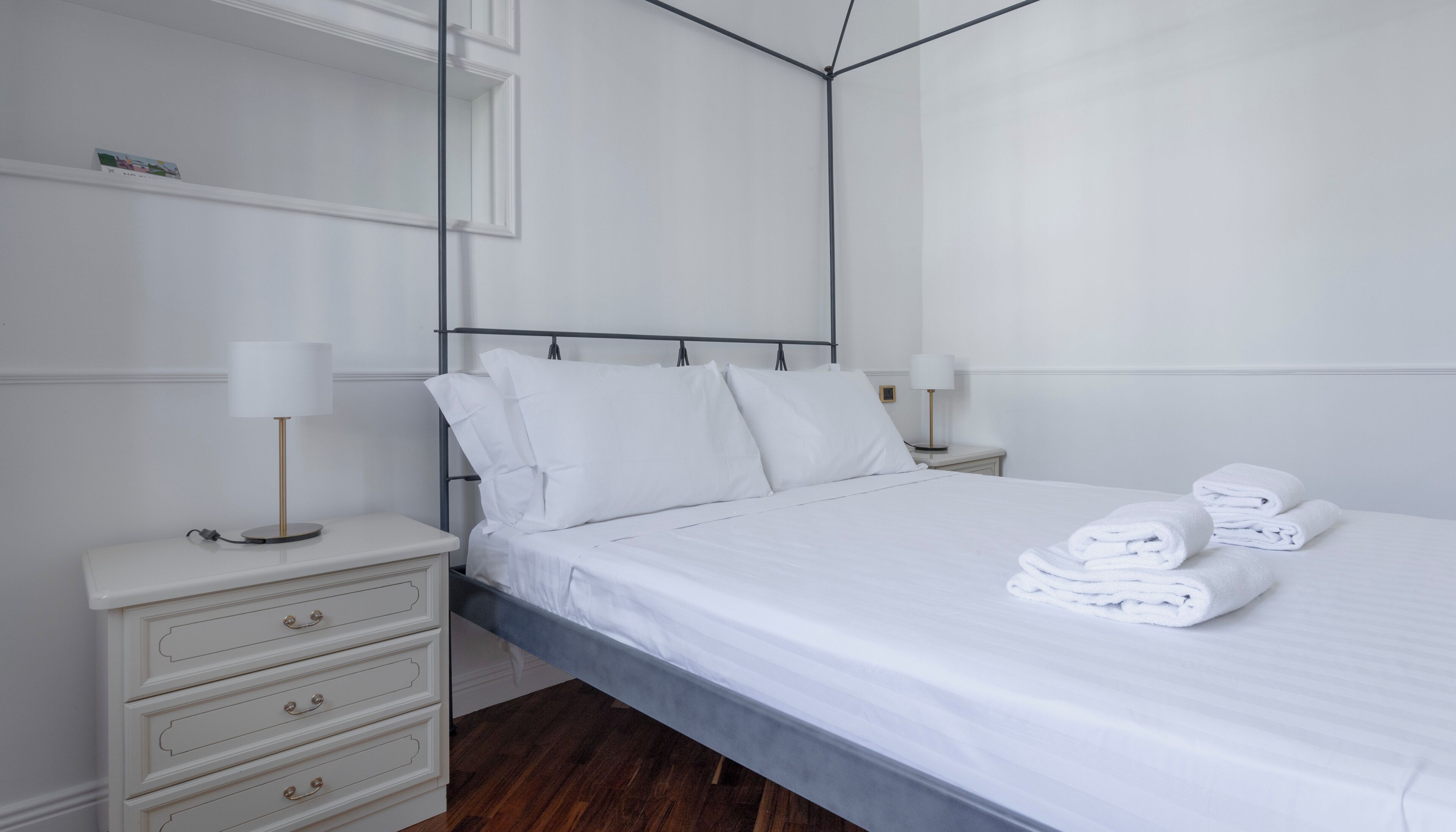 Moderni hotellihuone, jossa on siististi pedattu sänky, kaksi yöpöytää valaisimineen, lipasto ja suuri peili seinällä.