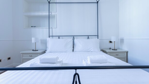 A neatly made bed with white linens and two towels, a bedside table with a lamp, and a wall-mounted shelf. - Italianway - Bodio 6 (Milan)