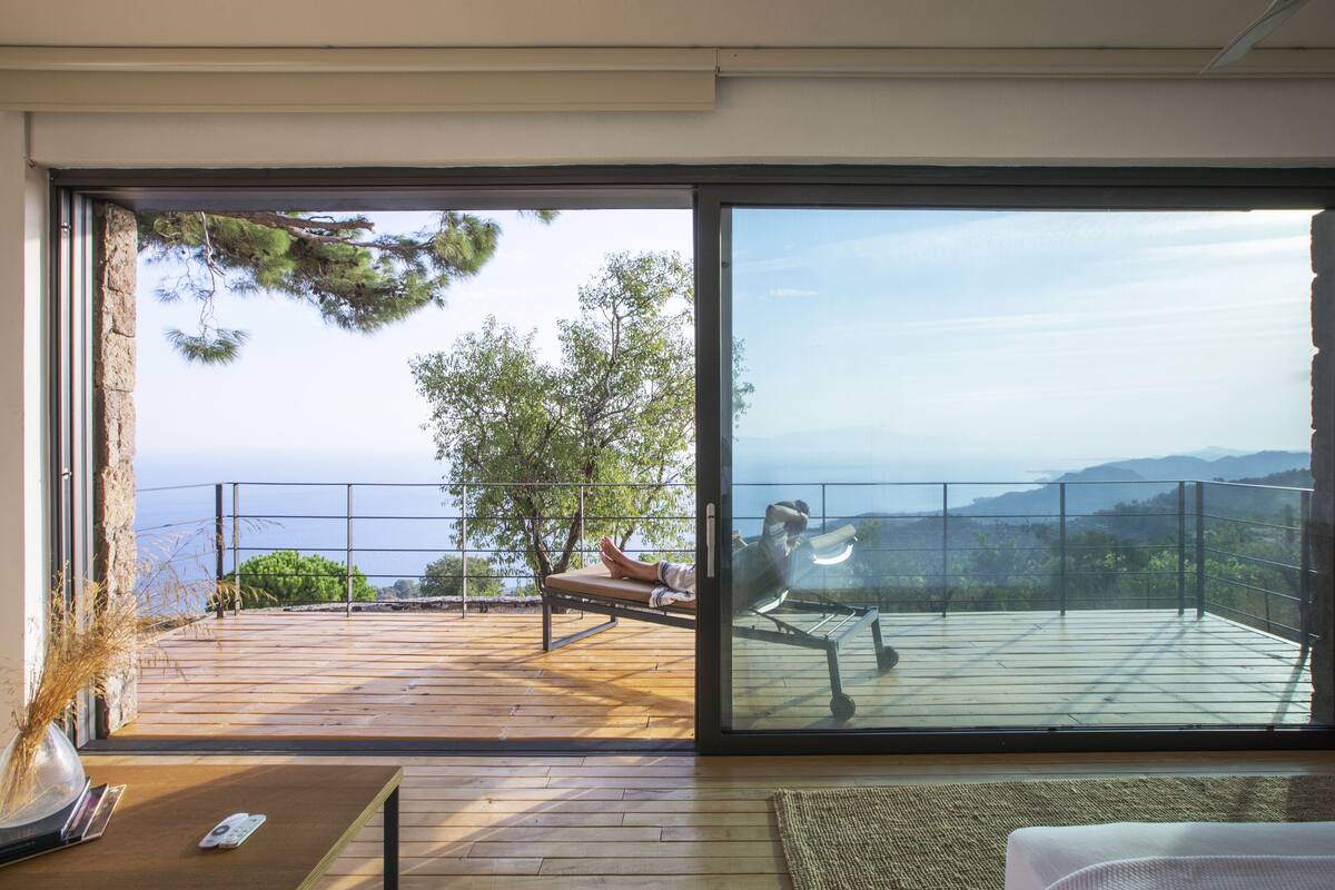 Une chambre moderne dotée d’une grande porte-fenêtre coulissante qui donne sur une terrasse extérieure offrant une vue sur la mer et les montagnes.