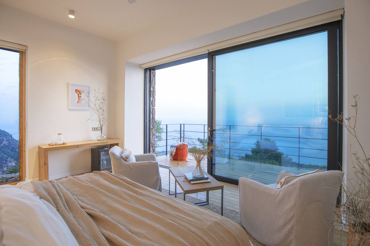 Une chambre moderne avec un grand lit, un bureau et une chaise, un balcon avec vue sur la mer et une grande fenêtre.