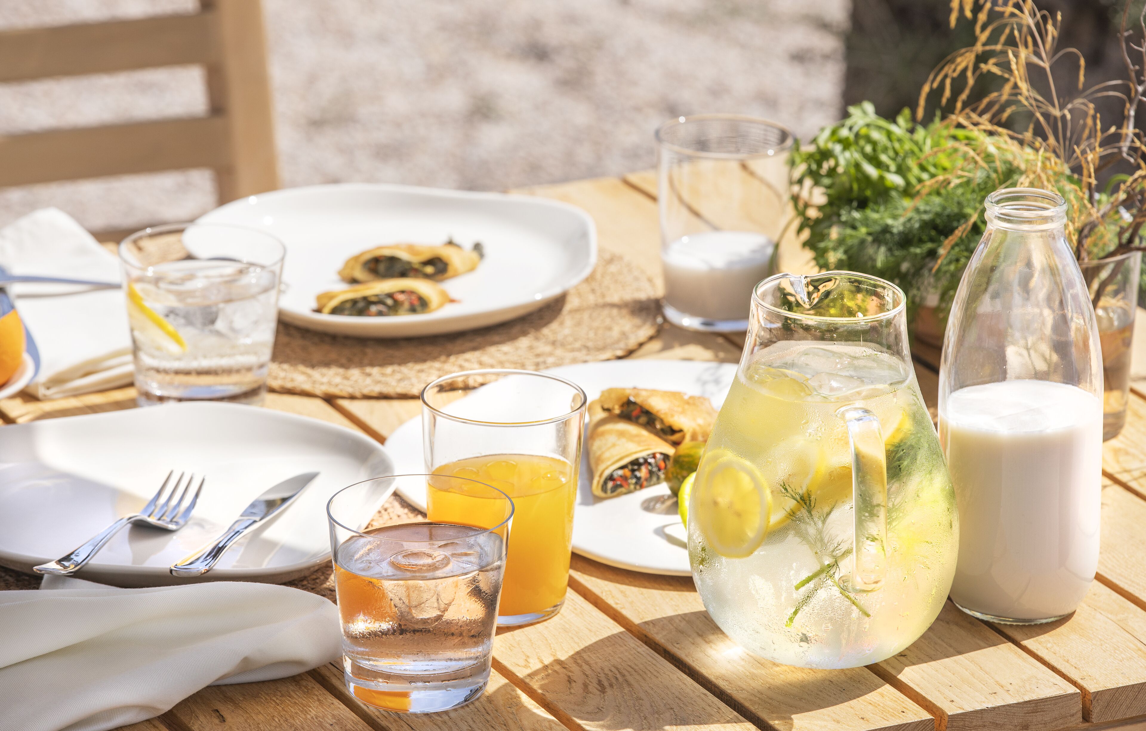 Une table dressée avec des assiettes, des verres et un pichet de thé glacé garni de rondelles de citron.