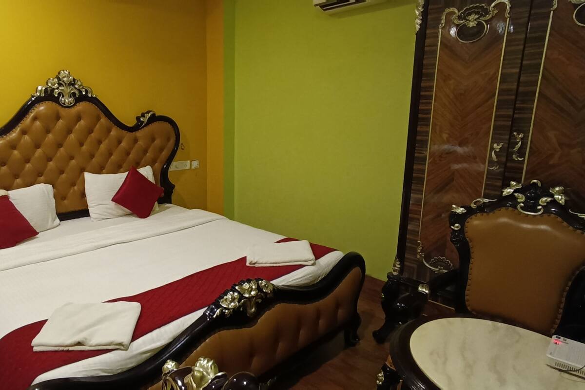 A neatly made bed with a tufted headboard, a bedside table with a telephone, and a mirror with ornate detailing.