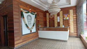 A reception area with a reception desk, a chandelier, and framed portraits on the walls. - N k Grand Days hotel (Port Blair)