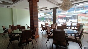A restaurant with multiple tables and chairs, a fire extinguisher on the wall, and a view of the street outside. - N k Grand Days hotel (Port Blair)