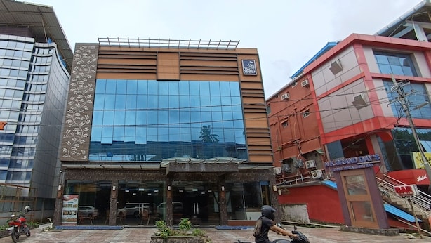 A modern building with a glass facade, a sign reading "VELOCITY," and a red building with a sign for "NKGRAND DAY'S." - N k Grand Days hotel (Port Blair)
