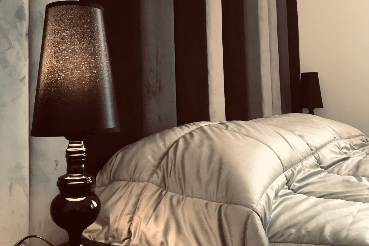 A bedroom with a bed, a nightstand, a lamp, and a wall with vertical stripes.