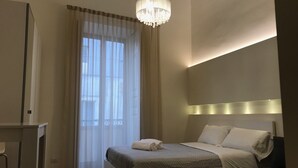 A bedroom with a bed, bedside table, and a chandelier. - Motta Palace Apartments and Rooms (Motta Sant'Anastasia)