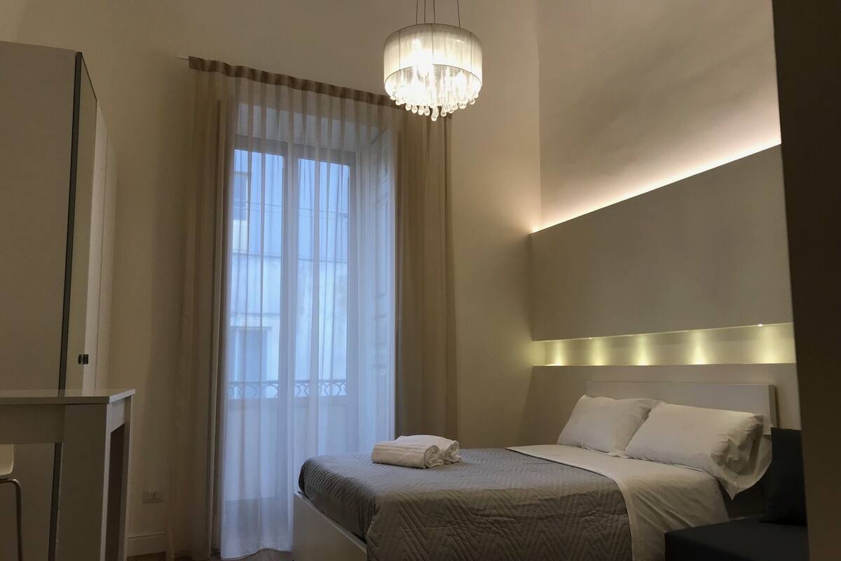 A bedroom with a bed, bedside table, and a chandelier.