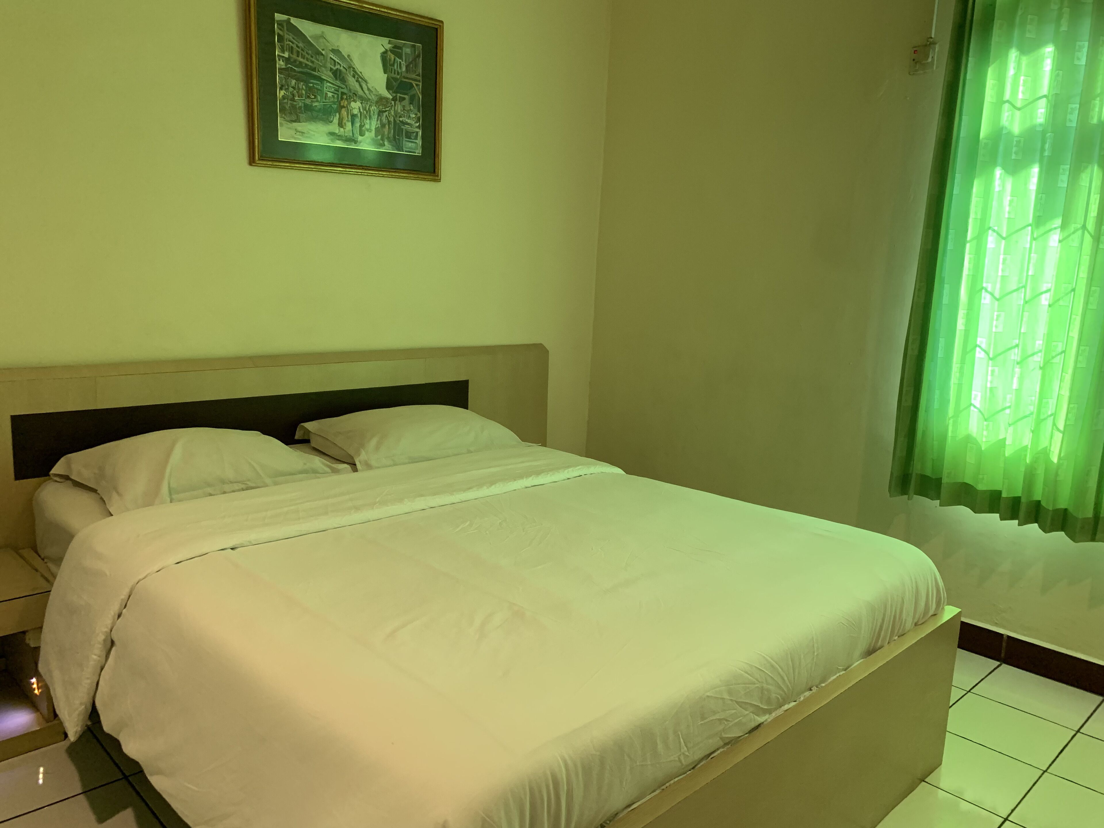 A neatly made bed with white bedding in a room with a green curtain and a framed picture on the wall.