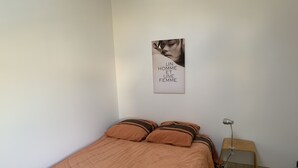 A bedroom with a bed, pillows, a bedside table, a lamp, and a wall with a framed picture.