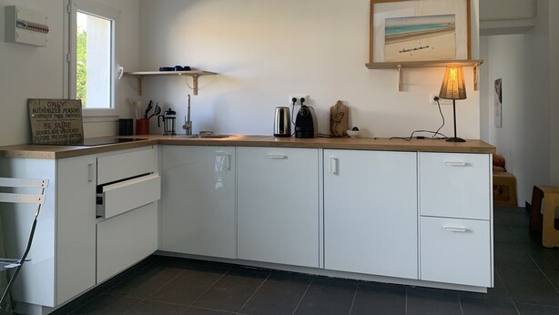 A modern kitchen with white cabinets, a wooden countertop, a coffee machine, and a painting above the sink.