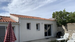 A house with a tiled roof, a sliding glass door, and a small patio with a wooden table and white plastic chairs.