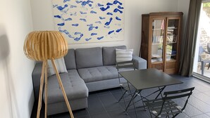 A modern living room with a grey sectional sofa, a wooden floor lamp, a glass cabinet, and a large abstract painting.