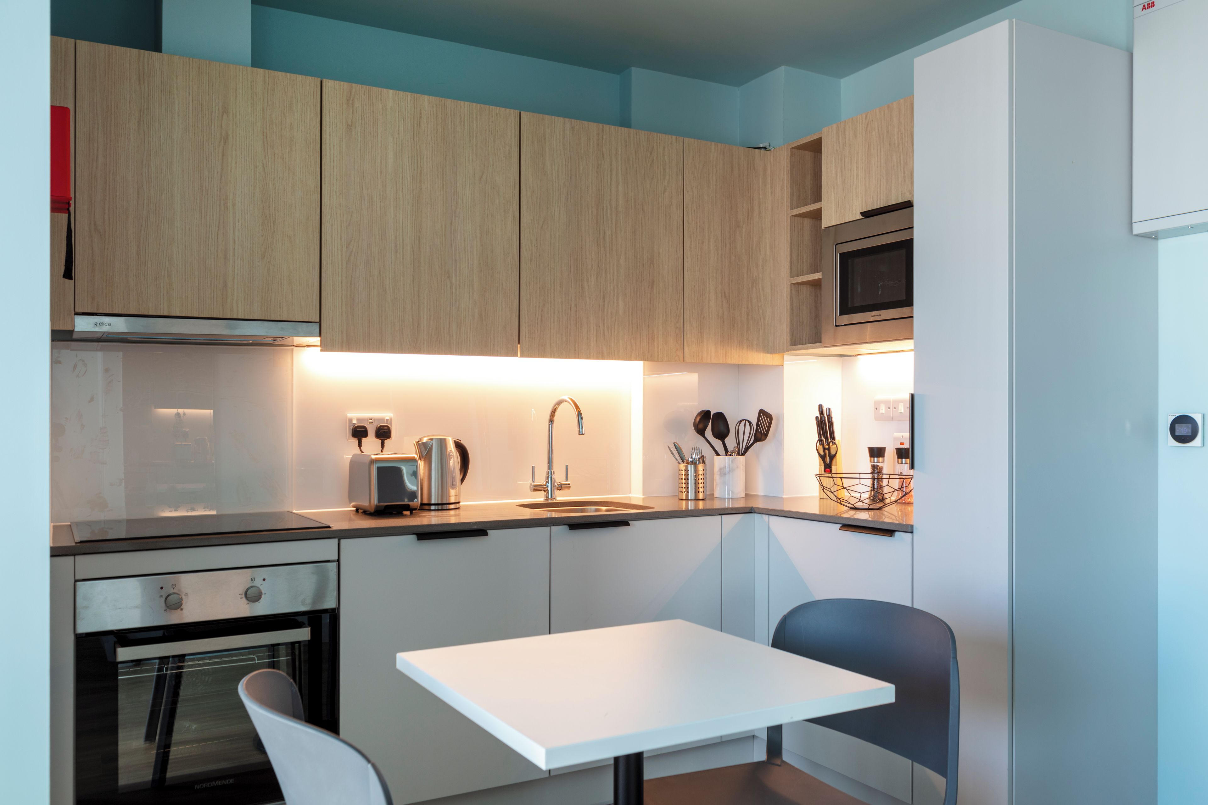 Una cucina moderna con mobili in legno, un forno a microonde integrato e un'area pranzo con tavolo e sedie bianche.