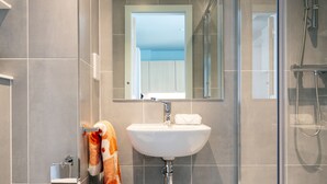 A modern bathroom with a glass-enclosed shower, a white sink, and a toilet. - Coleman Court Summer Apartments (Cork)