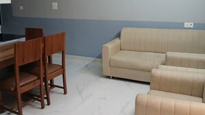 Un salón con un sofá color beige, una mesa de comedor de madera con sillas y un suelo de baldosas de color claro.