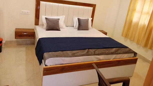 Un dormitorio ordenado con estructura de cama de madera, cabecera blanca y colcha azul oscuro.