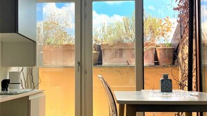 Una cocina moderna con una puerta de vidrio curva que da a un balcón, suelo de madera y sillas de plástico transparente.