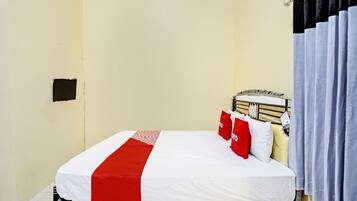 Una cama individual con colcha blanca y roja, cabecera y ventana con cortinas.