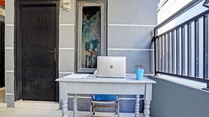 Un bureau blanc avec un ordinateur portable, une tasse bleue et une chaise devant une porte portant une plaque avec un numéro.