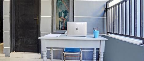 Un escritorio blanco con una laptop, una taza azul y una silla frente a una puerta con una placa numérica.
