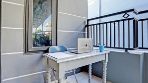Un balcon avec un bureau blanc, un ordinateur portable, une chaise et une tasse bleue.