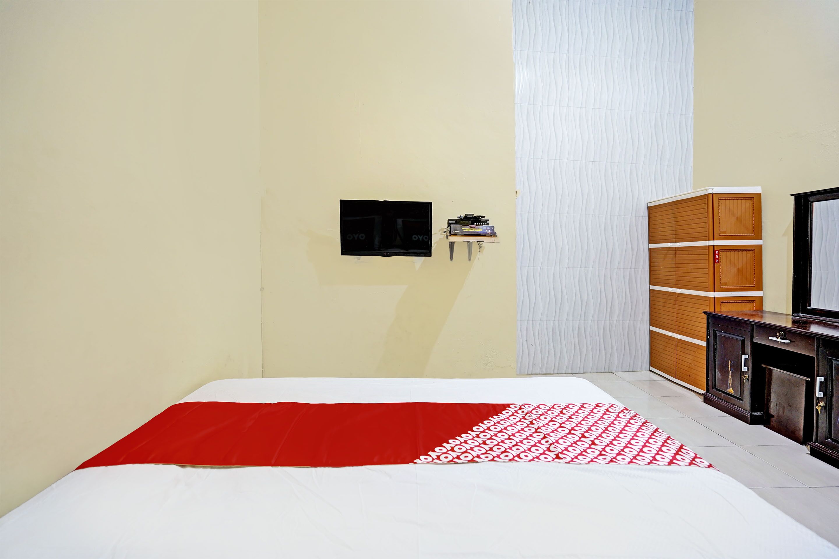 Une chambre à coucher comprenant un lit, une télévision, une armoire et une étagère fixée au mur.