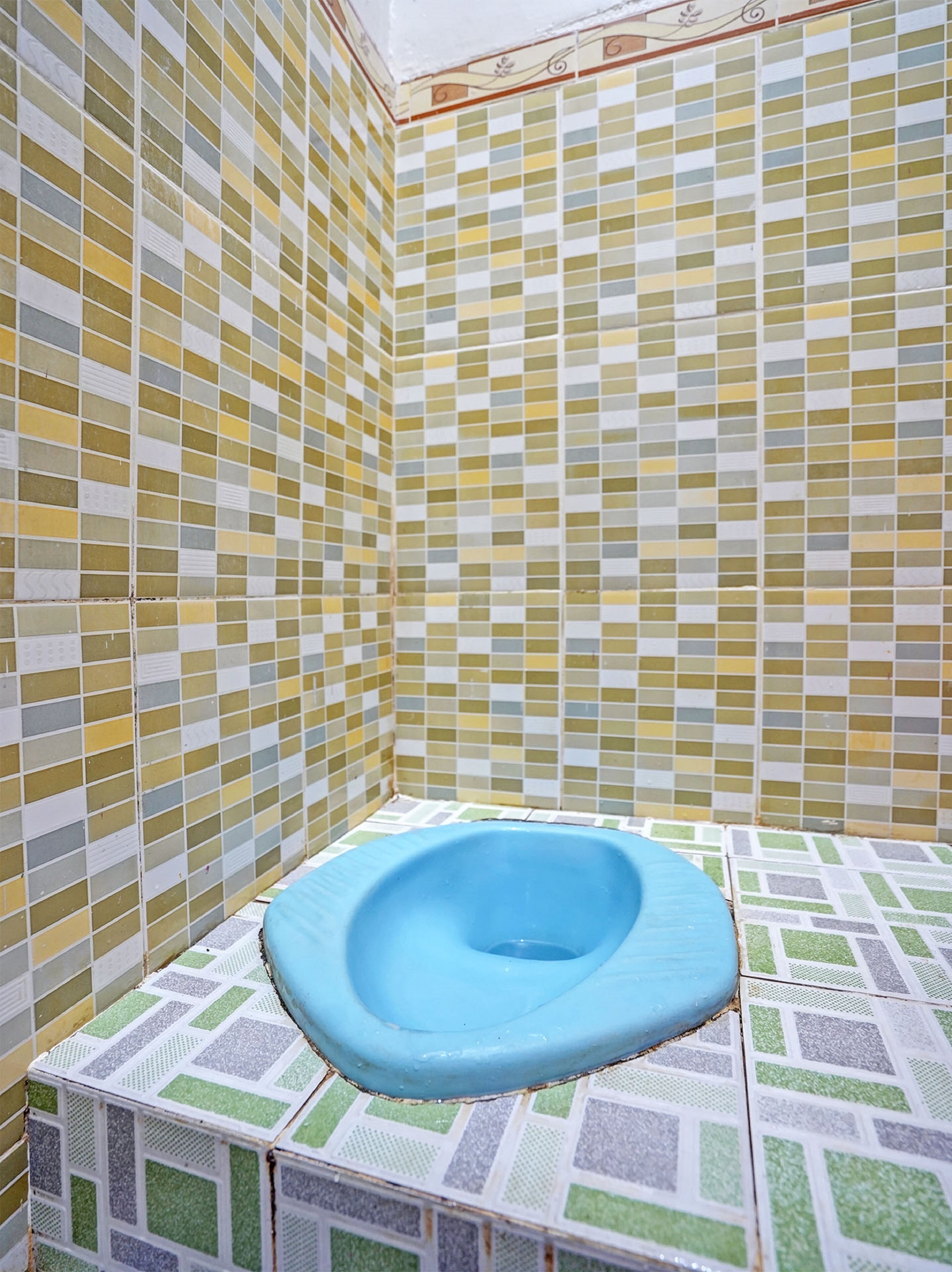 Une salle de bain avec des toilettes bleues, des murs et un sol carrelés.