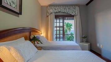 Une chambre d’hôtel avec deux lits, une fenêtre donnant sur un paysage verdoyant et un tableau encadré au mur.
