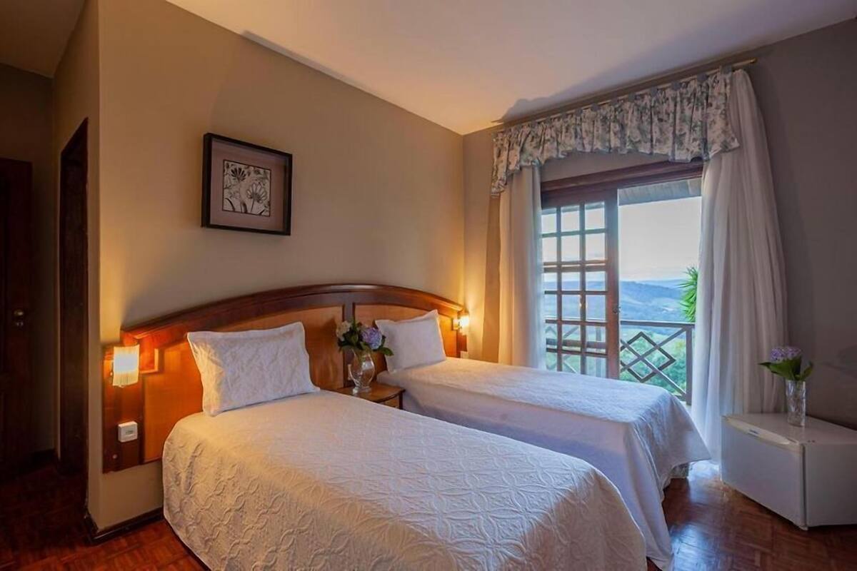Habitación de hotel con dos camas, cabecero de madera, un cuadro enmarco, ventana con cortinas y vistas al exterior.